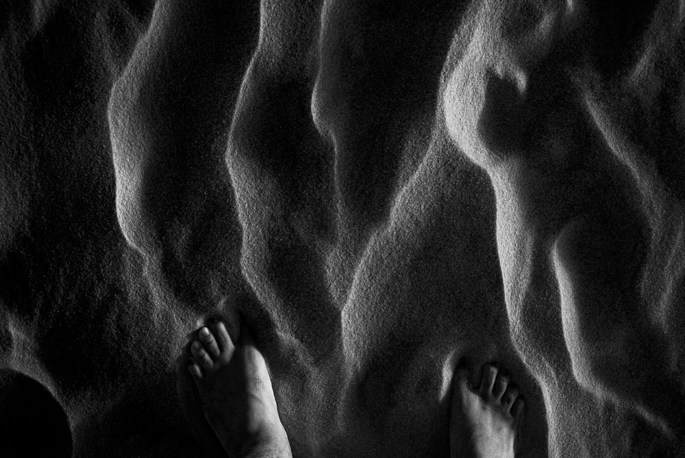 une photo en noir et blanc des pieds dans le sable d’une personne