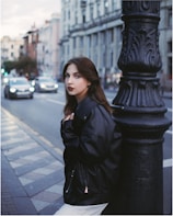 A young woman wearing a sleek Lumina Apparel jacket walking through a bustling city street at sunset.