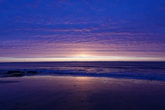 A serene beach scene at sunset with soft blue waves and white sand, reflecting the brand's color theme.