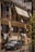 A residential building with balconies featuring metal railings and covered with retractable awnings. Air conditioning units are installed on the walls. Clothes are hanging to dry on a line outside the windows. In front of the building, a small car is parked. The scene is captured in bright, natural light, indicating a sunny day.