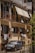 A residential building with balconies featuring metal railings and covered with retractable awnings. Air conditioning units are installed on the walls. Clothes are hanging to dry on a line outside the windows. In front of the building, a small car is parked. The scene is captured in bright, natural light, indicating a sunny day.