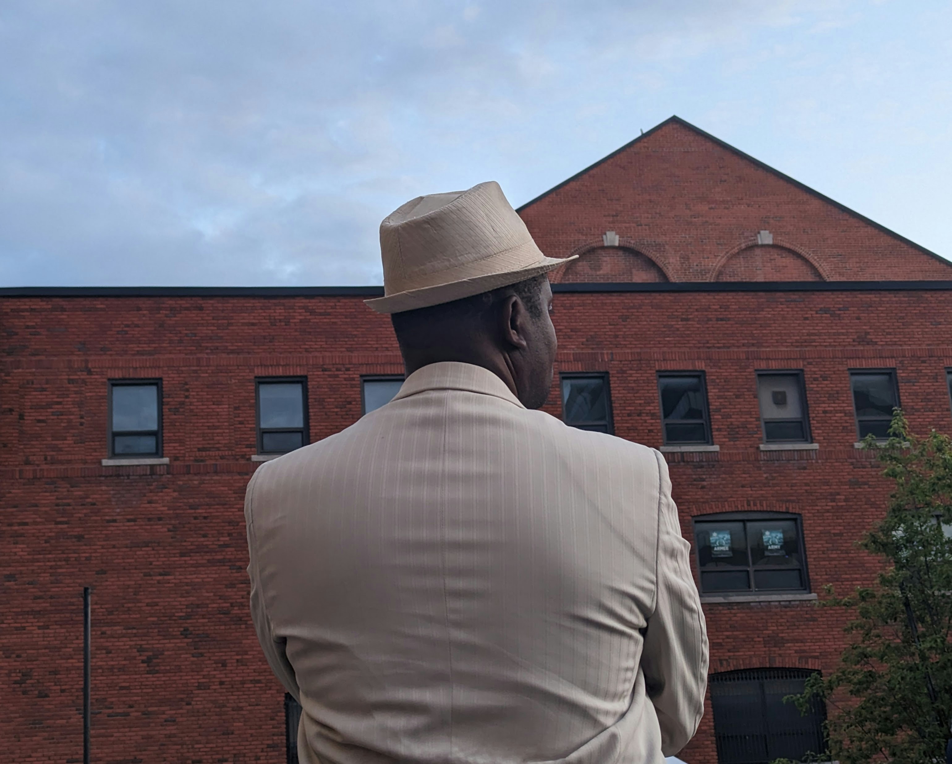 a man in a suit and hat standing in front of a brick building
