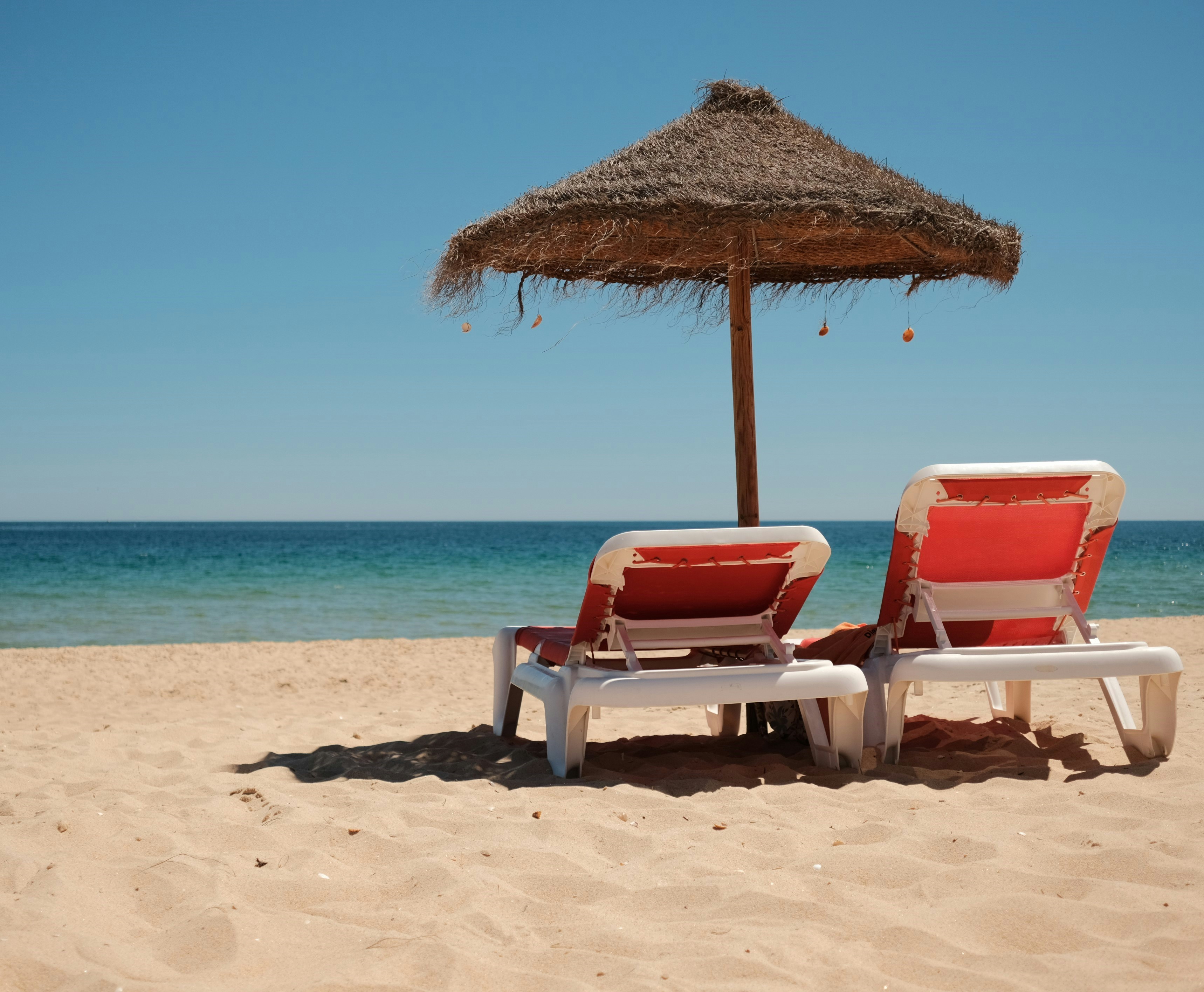 a couple of lawn chairs sitting on top of a sandy beach