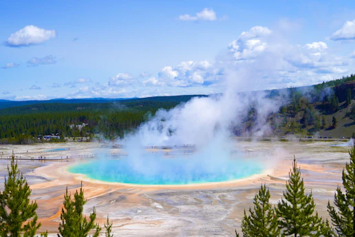 A vibrant sunrise over Old Faithful geyser erupting amidst the lush Yellowstone forest.