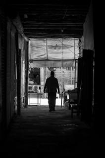 A silhouette of a lone figure walking down a narrow alley, framed by soft light and shadows.