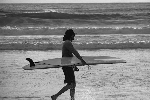 A peaceful moment capturing a surfer walking along the shoreline carrying a surfboard at sunset.