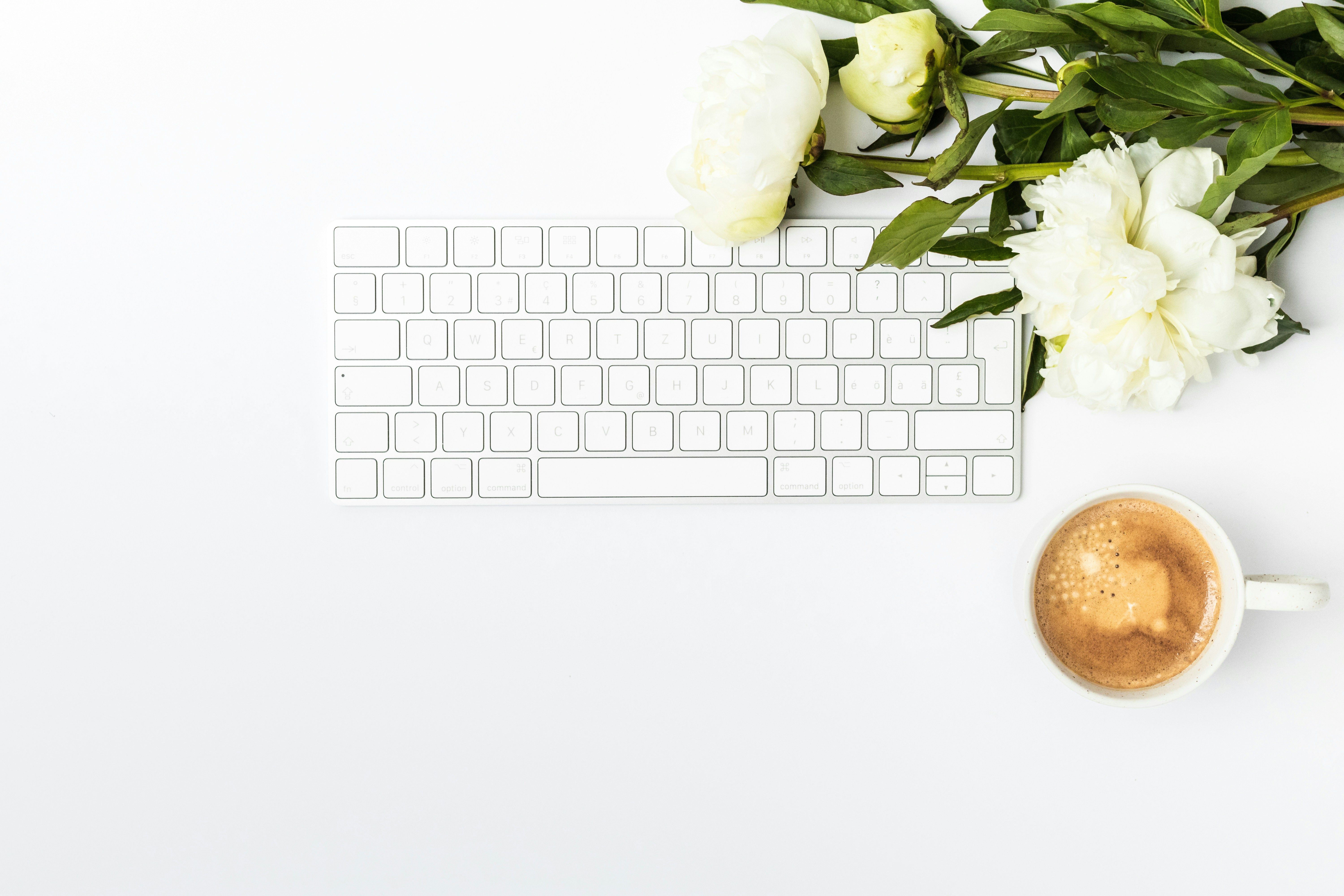 a cup of coffee next to a keyboard and flowers