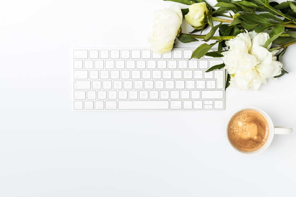 a cup of coffee next to a keyboard and flowers