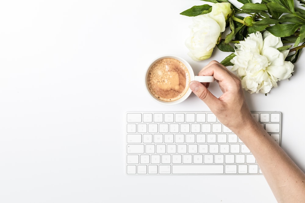 a person holding a cup of coffee next to a keyboard