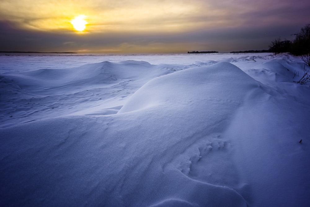 the sun is setting over a snow covered beach