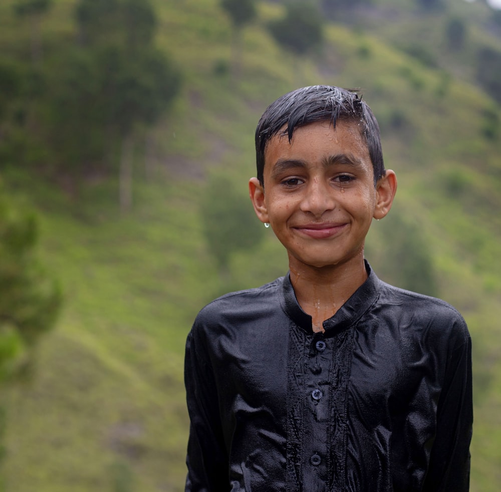 a young boy standing in front of a lush green hillside