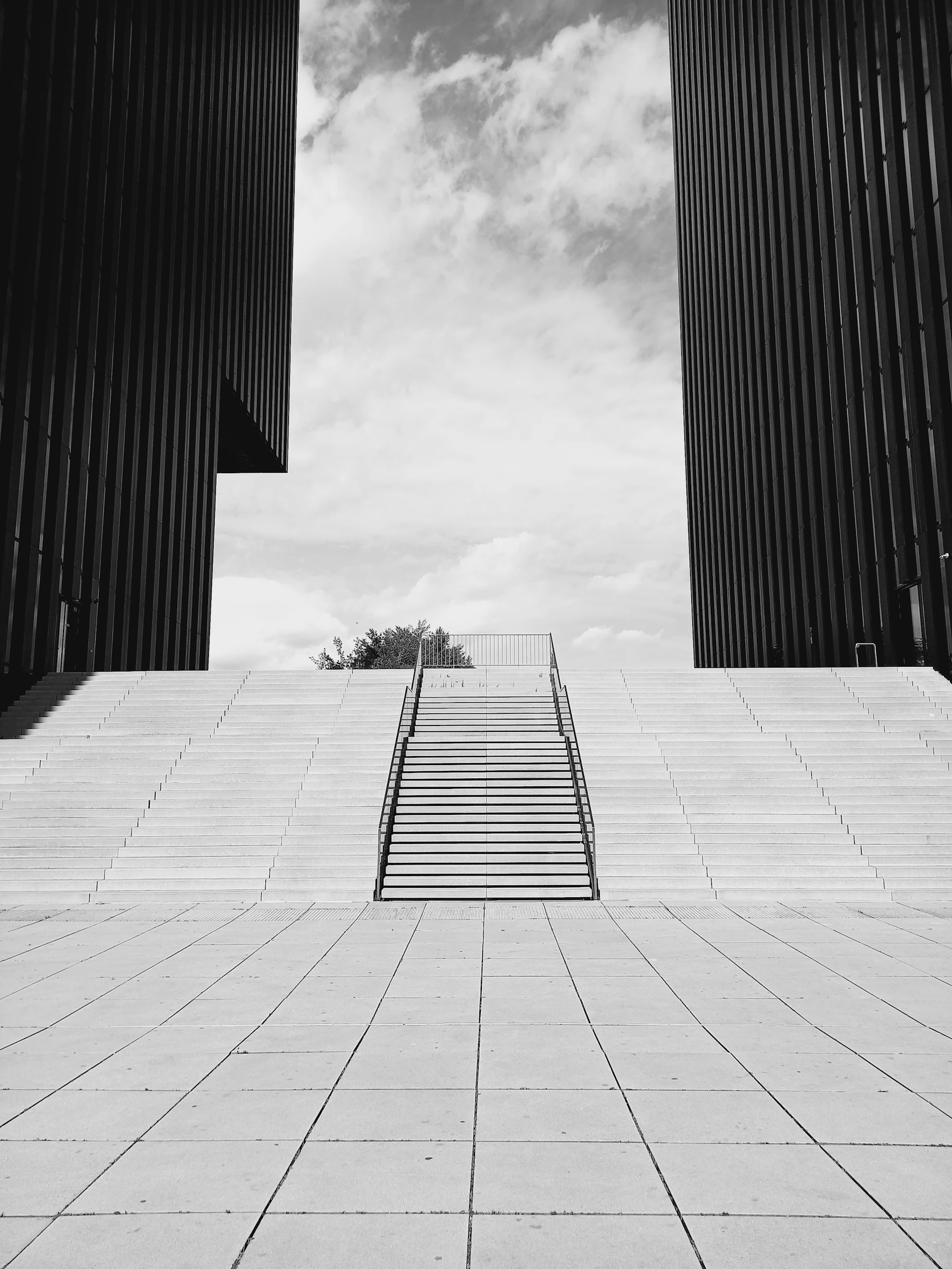 Concrete stairway rising between two dark buildings toward an open sky