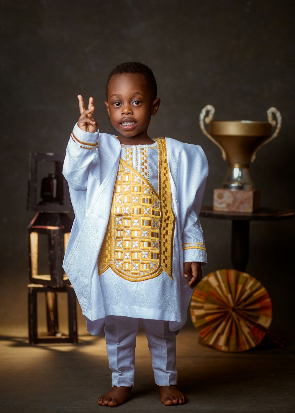a young boy dressed in a white and gold outfit