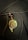 A pendant with an artistic design depicting a face, featuring various colors such as green, brown, and gold. The pendant hangs from a black cord alongside a glossy black bead, set against a dark textured background.