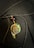 A pendant with an artistic design depicting a face, featuring various colors such as green, brown, and gold. The pendant hangs from a black cord alongside a glossy black bead, set against a dark textured background.