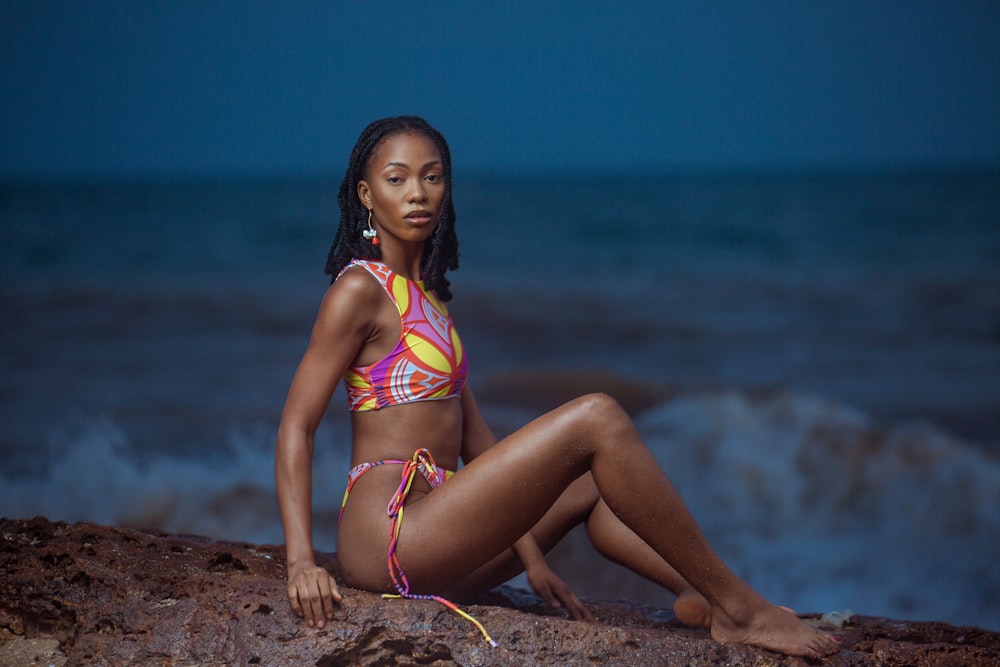 a woman in a bikini sitting on a rock near the ocean