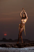 Model wearing a sleek, elegant swimsuit by the ocean at sunset.