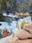 A vibrant mural on a wall features traditional Indian artwork. It includes colorful depictions of musicians playing instruments, dancers in cultural attire, and other folk elements. The backdrop includes detailed designs and additional smaller paintings. The mural is set amidst a natural environment with large trees and rock formations.
