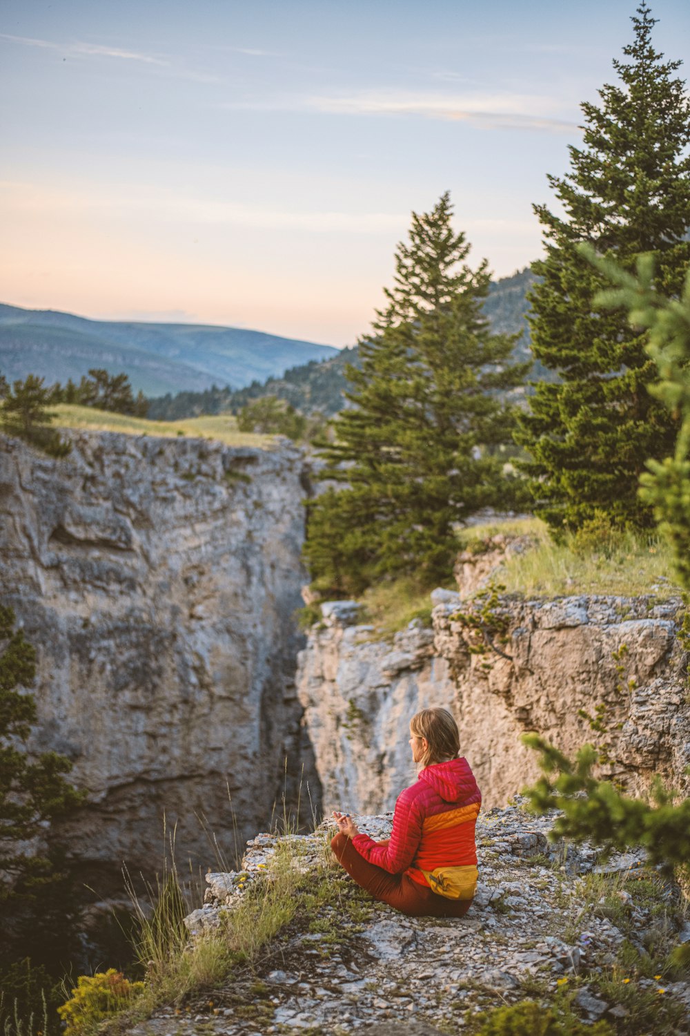 a person sitting on top of a cliff next to a forest