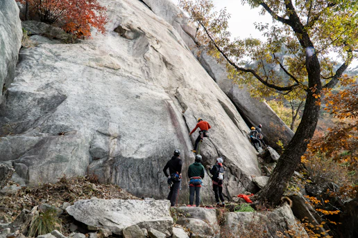 A group of climbers practicing rope handling on a natural rock face under instructor guidance.