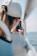 A person wearing a white cap is holding a smartphone and capturing a photo or video, with a blurred view of water in the background and an aluminum railing next to them.