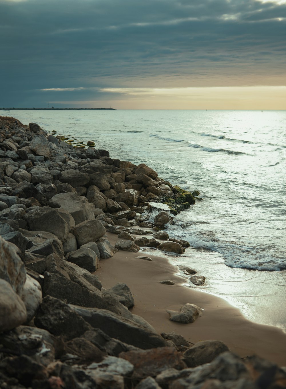 a beach with rocks and water under a cloudy sky