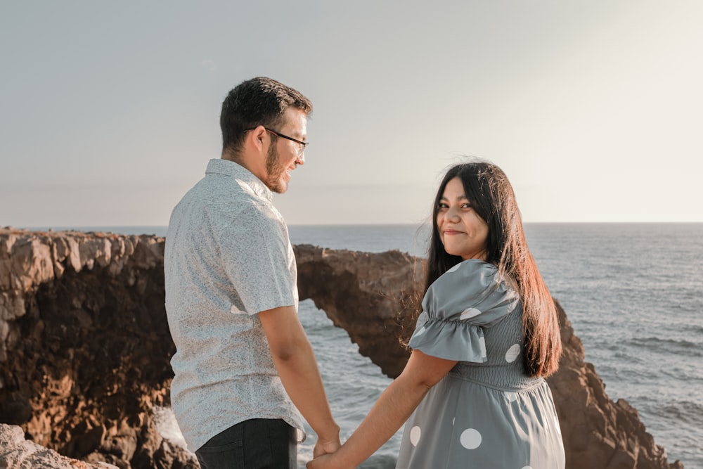 a man and a woman holding hands near the ocean