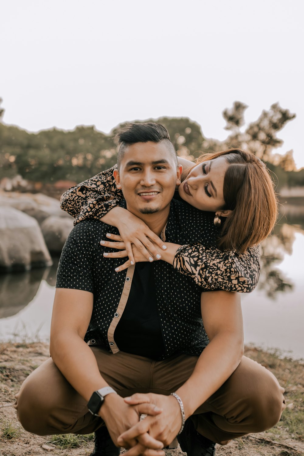 a man holding a woman on his back in front of a body of water