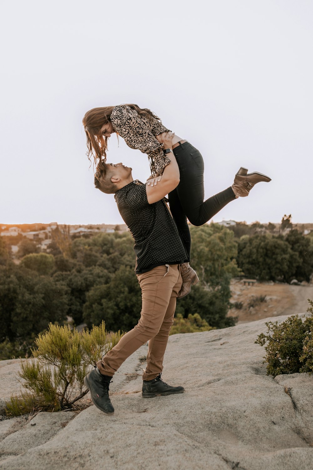 a man holding a woman on top of a rock