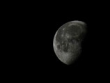 A detailed, close-up view of the moon with visible craters and surface texture. The moon appears partially illuminated against a deep black background, highlighting its crescent shape.