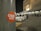 A sticker labeled 'Wish 107.5' is affixed to a gray pole in a nighttime setting. In the background, there is a parking lot with a white car and a crowd of people near the entrance of a building that has visible signage and lights.