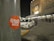 A sticker labeled 'Wish 107.5' is affixed to a gray pole in a nighttime setting. In the background, there is a parking lot with a white car and a crowd of people near the entrance of a building that has visible signage and lights.