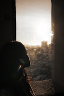 A silhouette of a person looking out a window, with golden hour light creating a peaceful ambiance.