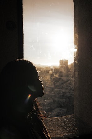 A silhouette of a person looking out a window, with golden hour light creating a peaceful ambiance.