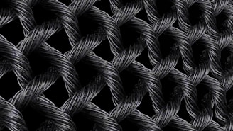 Interwoven strands of dark, metallic wires form a textured, lattice-like pattern. The intricate braiding creates a sense of depth and complexity, with highlights emphasizing the reflective surface of the materials.