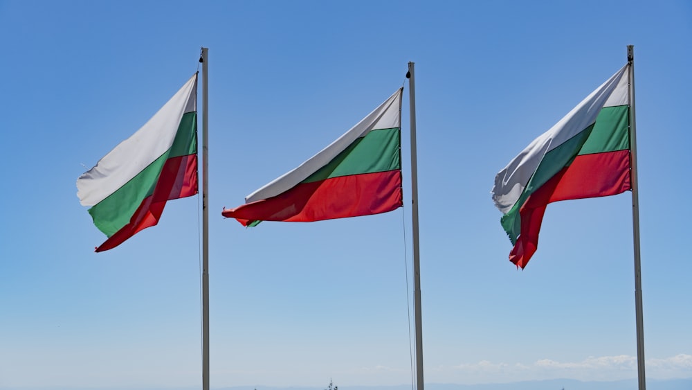 three flags flying in the wind on a sunny day