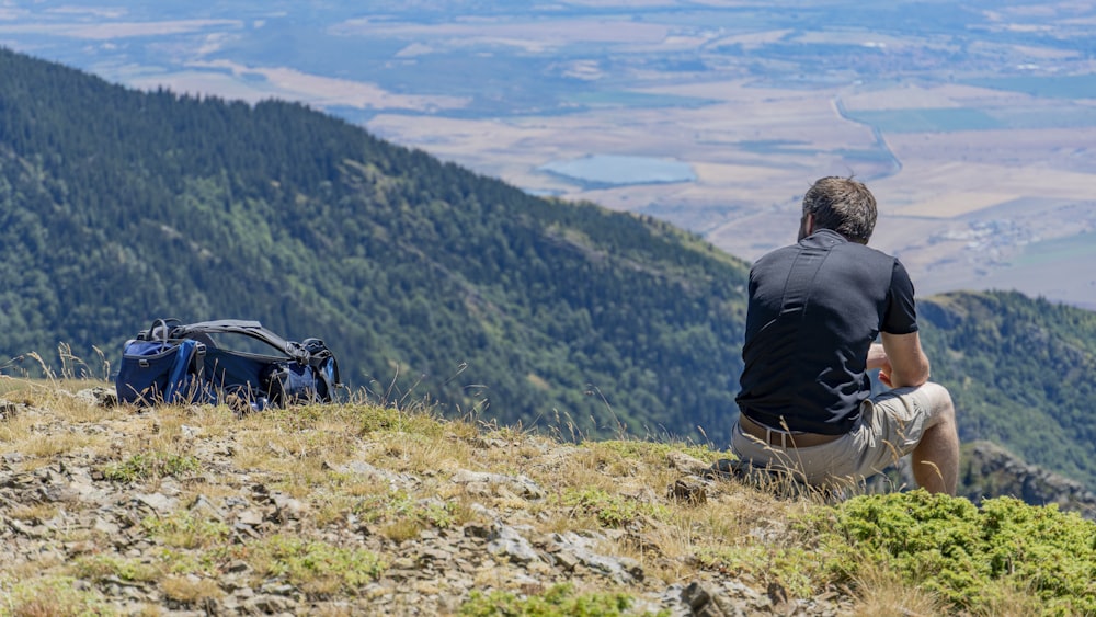 a man sitting on top of a hill next to a backpack