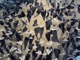 A multitude of white paper airplanes are suspended against a wall, casting intricate shadows. The airplanes are arranged at different angles, creating a dynamic and visually engaging pattern. The play of light and shadow adds depth and complexity to the scene.