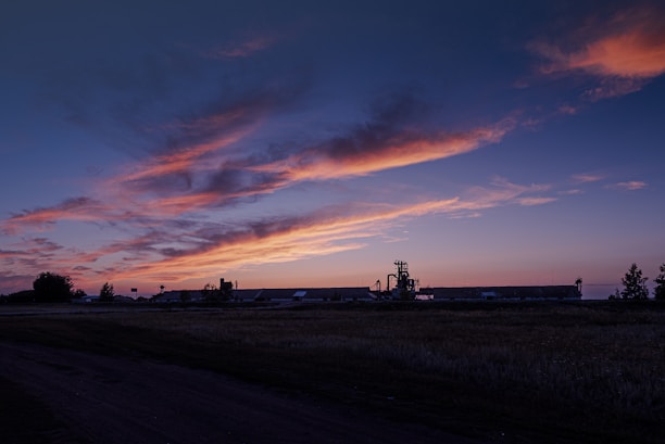A panoramic view of an industrial gas plant at sunset with vibrant orange and purple skies.