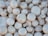 A collection of fresh white button mushrooms piled closely together, displaying a natural earthy texture with some speckles of soil visible on their surfaces.