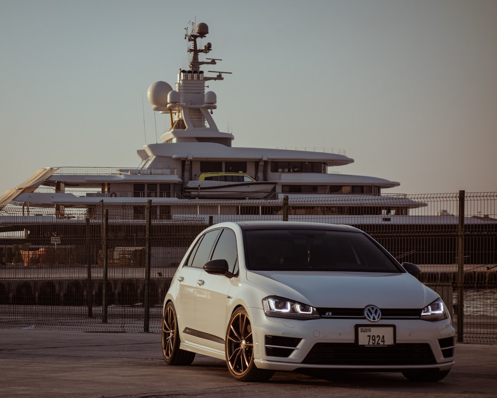 a white car parked in front of a large boat