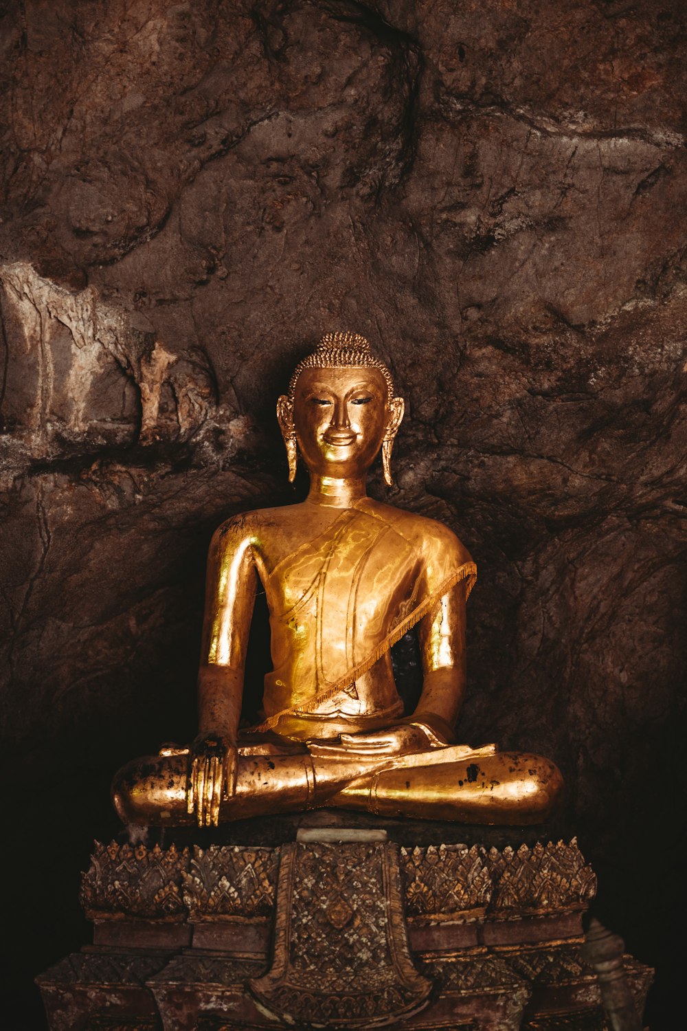 Una statua dorata del Buddha seduta in una grotta