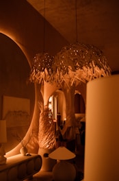 Warm ambient lighting fills a room decorated with stylish, organic-shaped furniture and accent pieces. Hanging woven light fixtures create a cozy atmosphere, with matching sculptures and vases enhancing the design. Archways and soft shadows add depth and intrigue to the setting.