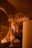Warm ambient lighting fills a room decorated with stylish, organic-shaped furniture and accent pieces. Hanging woven light fixtures create a cozy atmosphere, with matching sculptures and vases enhancing the design. Archways and soft shadows add depth and intrigue to the setting.