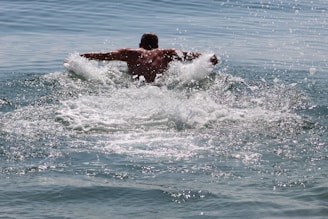 A close-up of a swimmer slicing through calm sea water, droplets sparkling in the sunlight around her.
