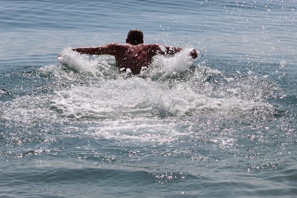 A close-up of a swimmer slicing through calm sea water, droplets sparkling in the sunlight around her.
