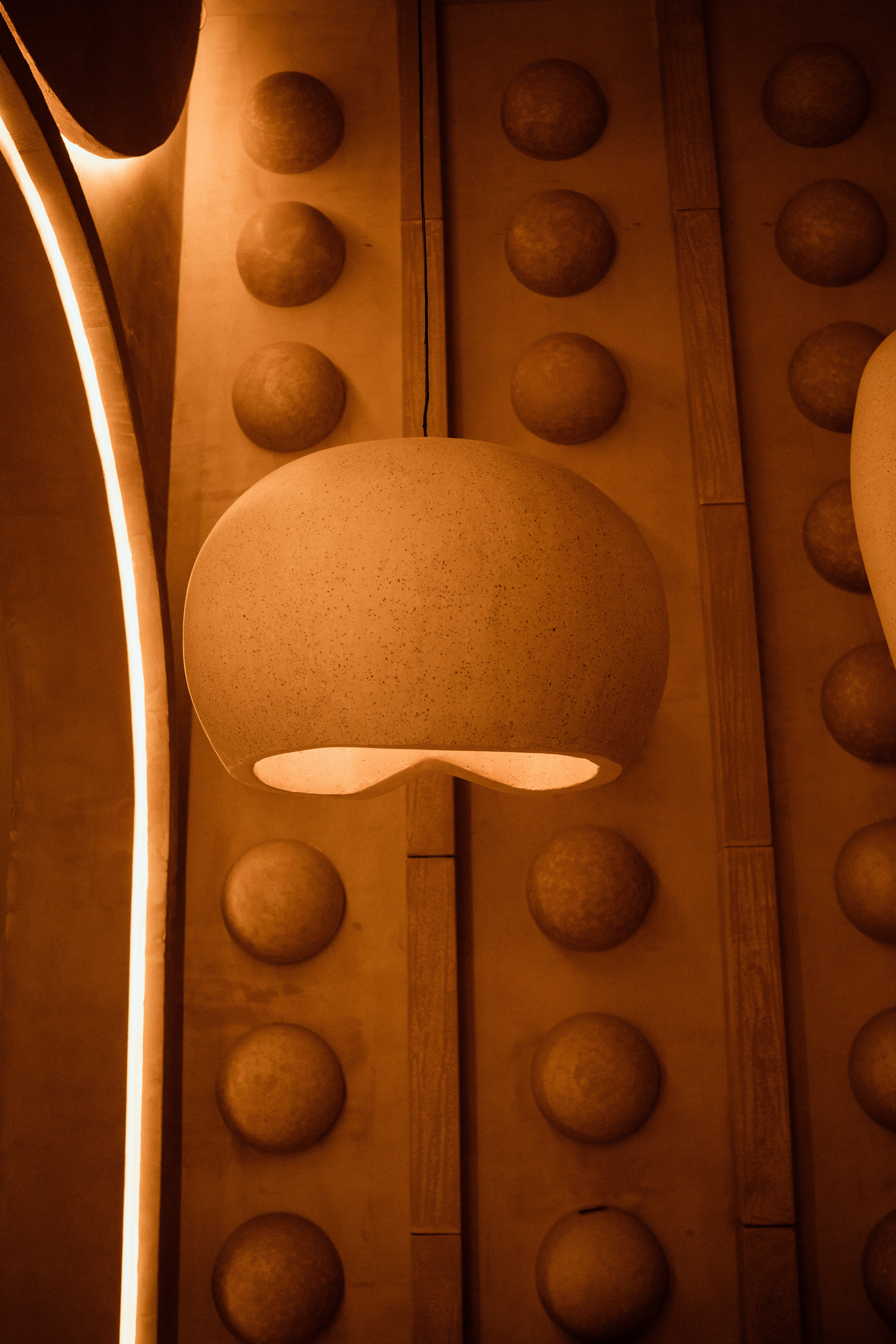Speckled pendant light hangs against a textured wooden wall panel.