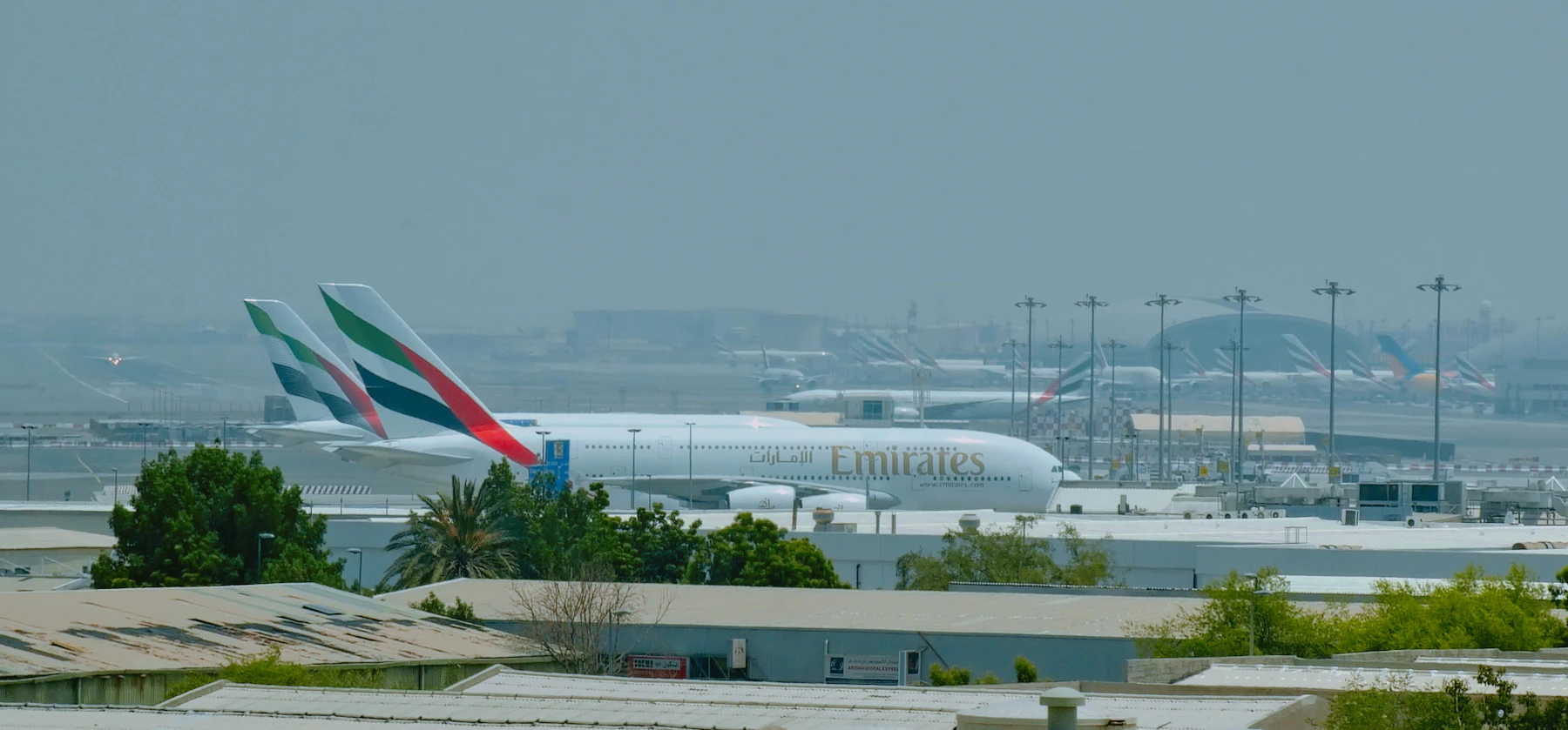 Travel photograph: An Emirates passenger aircraft stands at Dubai International Airport beneath a pale, hazy sky.