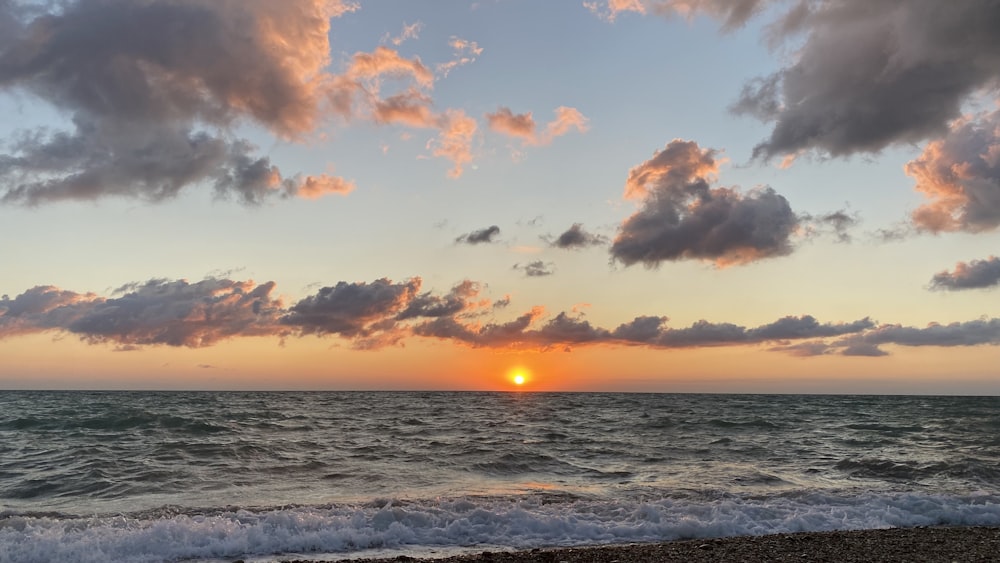 the sun is setting over the ocean on a cloudy day