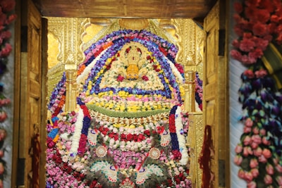 An elaborate floral arrangement adorns a richly decorated area with symmetrical patterns and detailed designs. The structure appears golden with intricate carvings, and the vast array of flowers includes pink, red, purple, and white tones, tightly packed together to form a visually stunning display.